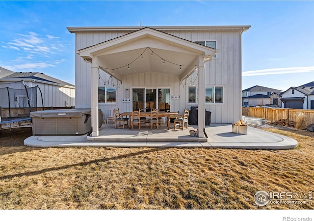 back of house with board and batten siding, a patio area, fence, and a trampoline