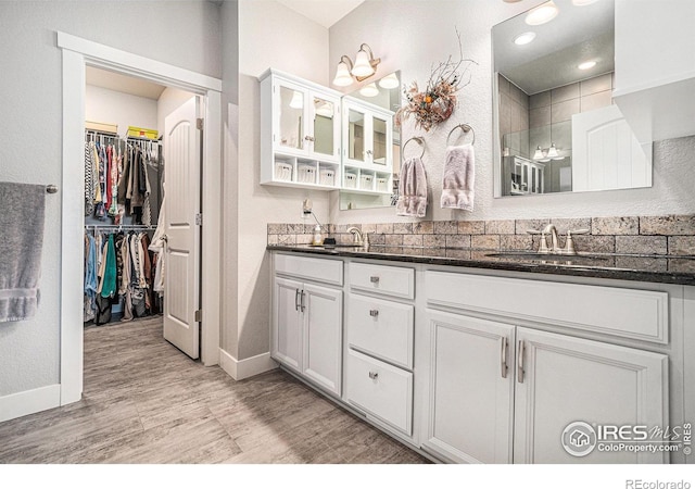 full bathroom featuring double vanity, a walk in closet, a sink, and wood finished floors