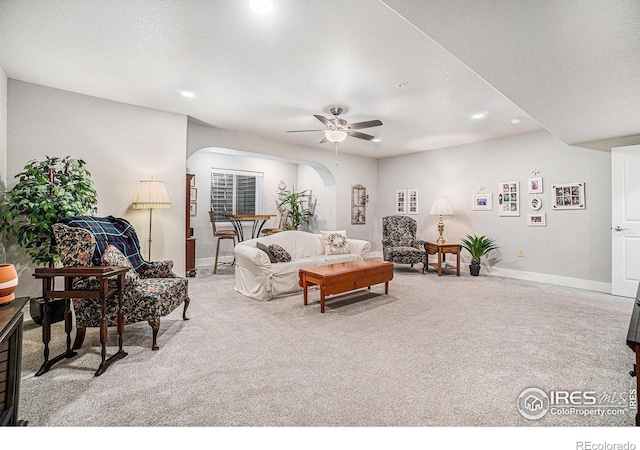 living area with arched walkways, light carpet, and baseboards