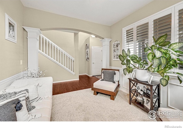 sitting room with decorative columns, stairs, arched walkways, and wood finished floors