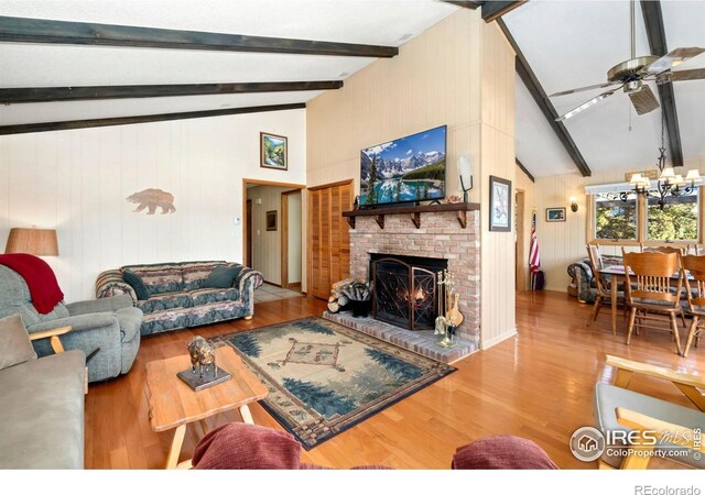 living area with lofted ceiling with beams, ceiling fan with notable chandelier, a fireplace, and wood finished floors