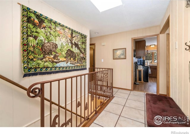 hall featuring a skylight, light tile patterned floors, and an upstairs landing