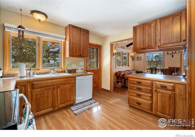 kitchen featuring dishwasher, brown cabinets, light wood-style floors, a sink, and range with electric stovetop