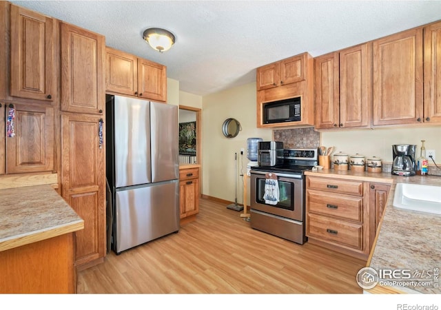 kitchen featuring light wood-style floors, appliances with stainless steel finishes, light countertops, and a textured ceiling