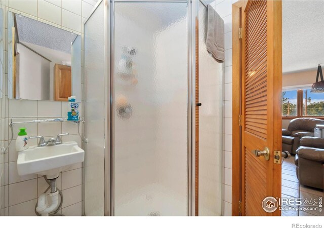 full bath with a textured ceiling, a sink, tile walls, backsplash, and a stall shower
