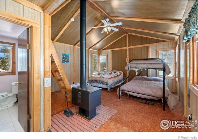 bedroom featuring a wood stove, multiple windows, wooden walls, and lofted ceiling with beams