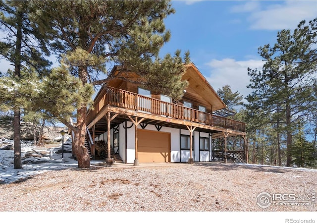 rear view of house featuring driveway, an attached garage, stairs, a deck, and stucco siding