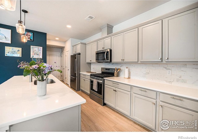 kitchen with appliances with stainless steel finishes, light wood-type flooring, decorative backsplash, and gray cabinetry