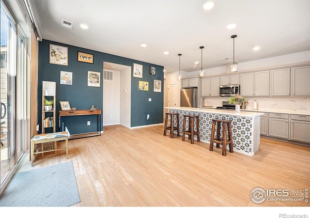 kitchen with a kitchen island with sink, gray cabinetry, stainless steel appliances, a kitchen breakfast bar, and light wood finished floors