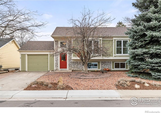 tri-level home with a garage, stone siding, roof with shingles, and concrete driveway