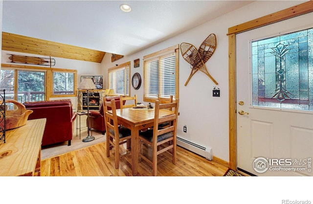 dining area featuring vaulted ceiling, wood finished floors, a baseboard radiator, and a fireplace