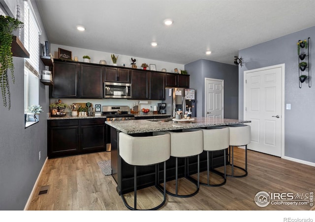 kitchen featuring stainless steel appliances, a breakfast bar, light wood-style flooring, and visible vents