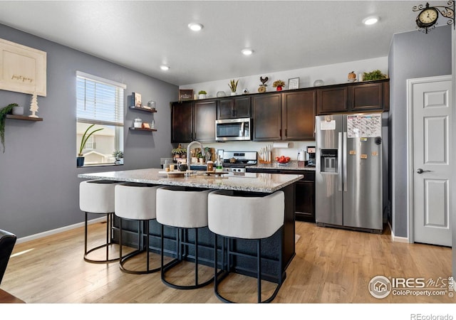 kitchen featuring dark brown cabinetry, an island with sink, light wood-style flooring, appliances with stainless steel finishes, and a kitchen breakfast bar