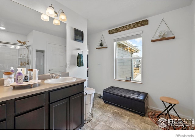 bathroom featuring stone finish flooring, an enclosed shower, vanity, and baseboards