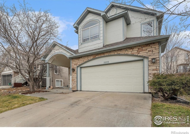 traditional-style house featuring a garage, stone siding, and concrete driveway