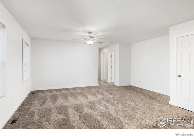 carpeted spare room featuring baseboards, visible vents, and a ceiling fan