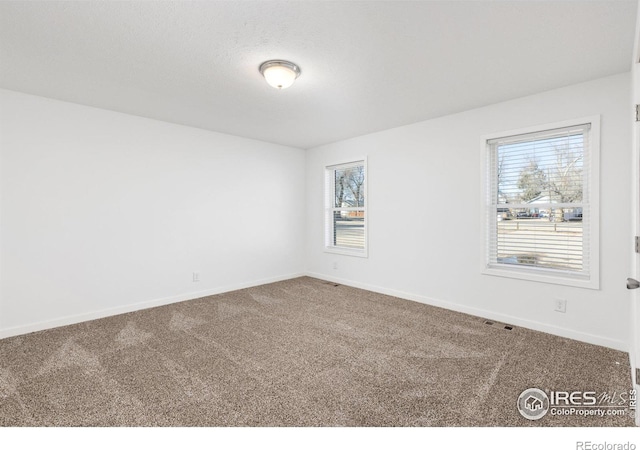 unfurnished room with carpet, visible vents, and baseboards