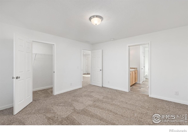 unfurnished bedroom featuring baseboards, a walk in closet, connected bathroom, and light colored carpet