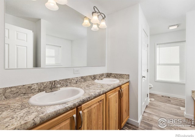 bathroom with wood finished floors, a sink, toilet, and double vanity