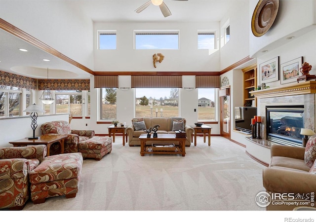 living area with carpet floors, built in shelves, a high end fireplace, ceiling fan, and baseboards