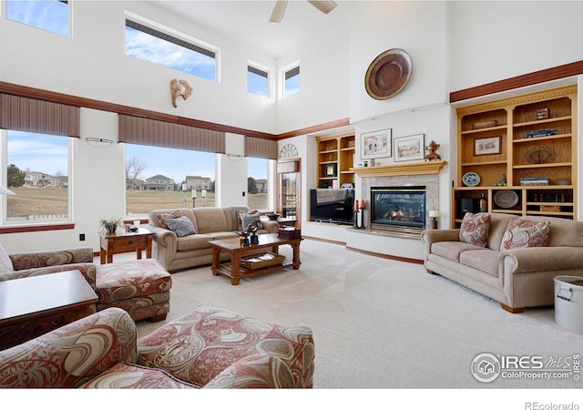 carpeted living area with built in shelves, a towering ceiling, a glass covered fireplace, ceiling fan, and a wall mounted air conditioner