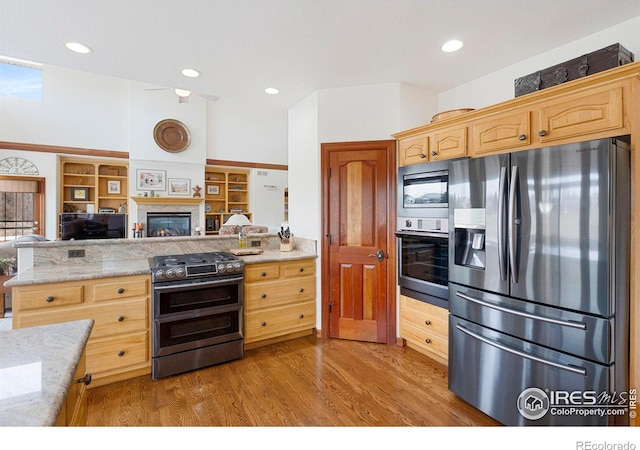 kitchen featuring a glass covered fireplace, appliances with stainless steel finishes, open floor plan, light brown cabinetry, and light wood-style floors