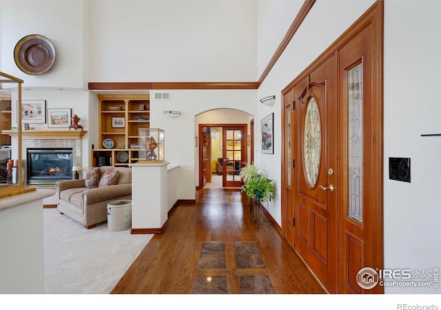 foyer featuring a towering ceiling, visible vents, dark wood finished floors, and a glass covered fireplace