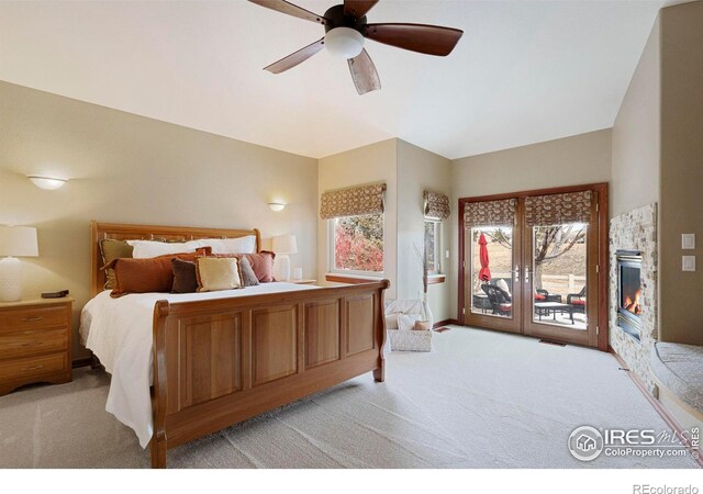 bedroom with a lit fireplace, a ceiling fan, light colored carpet, and access to exterior