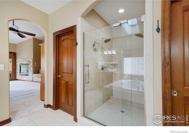 bathroom with a ceiling fan, a stall shower, a multi sided fireplace, and tile patterned floors