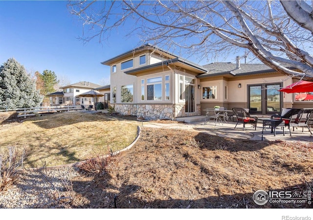 back of house with stone siding, a patio area, fence, and stucco siding