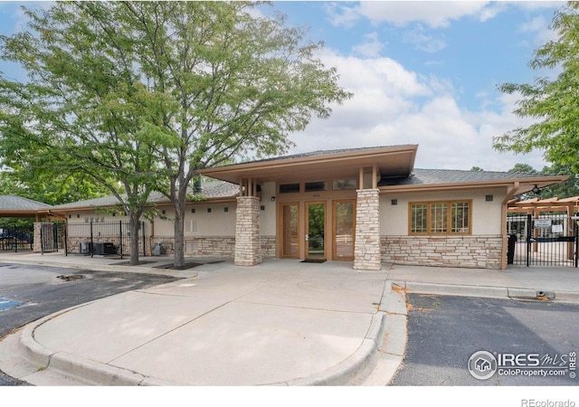 prairie-style house featuring stone siding, fence, and stucco siding