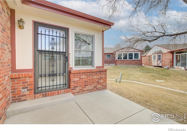 view of exterior entry with brick siding and a lawn