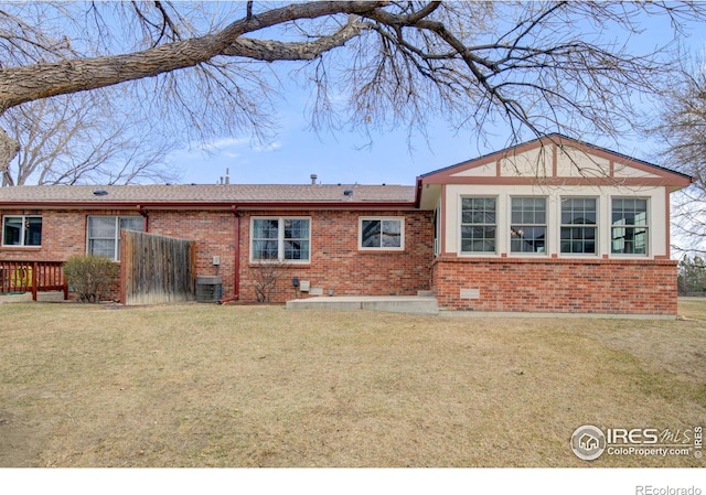 rear view of house with brick siding, a lawn, central AC, and fence