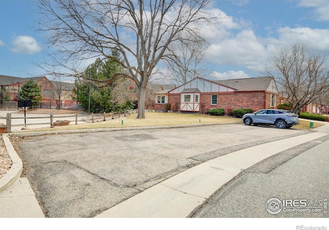 view of front of house featuring uncovered parking, brick siding, a front lawn, and fence