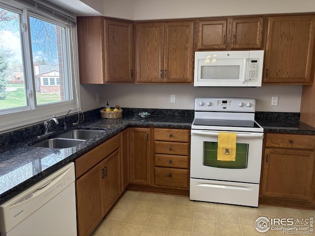 kitchen with brown cabinetry, a sink, white appliances, and plenty of natural light