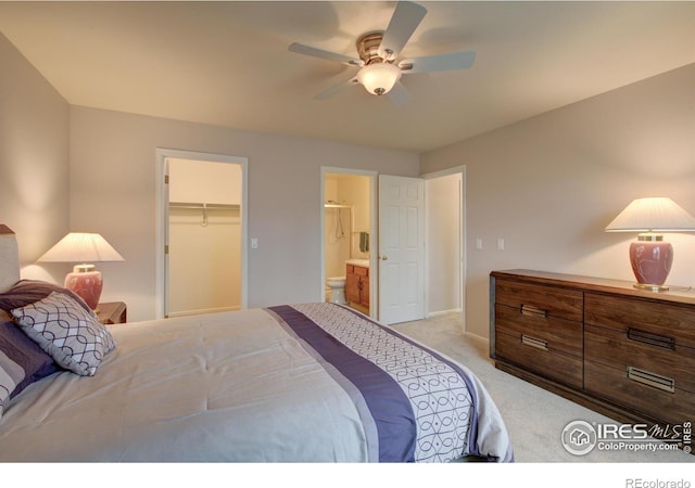 bedroom with a ceiling fan, connected bathroom, a walk in closet, light carpet, and baseboards