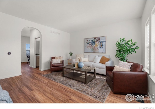 living room featuring baseboards, visible vents, arched walkways, and wood finished floors