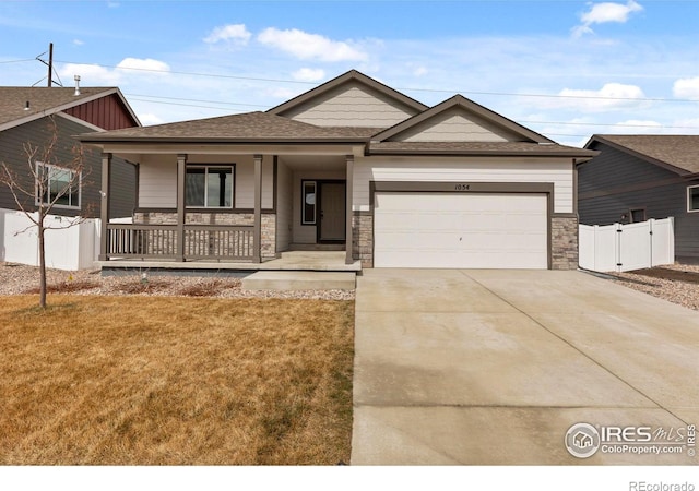 view of front of home featuring a porch, an attached garage, fence, stone siding, and driveway