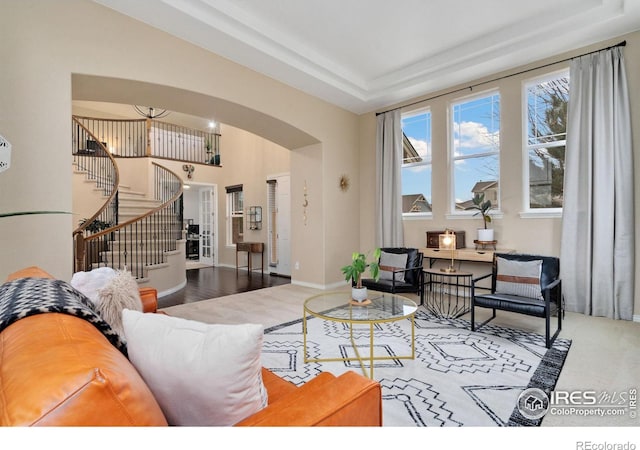 living area featuring arched walkways, stairway, a raised ceiling, and baseboards