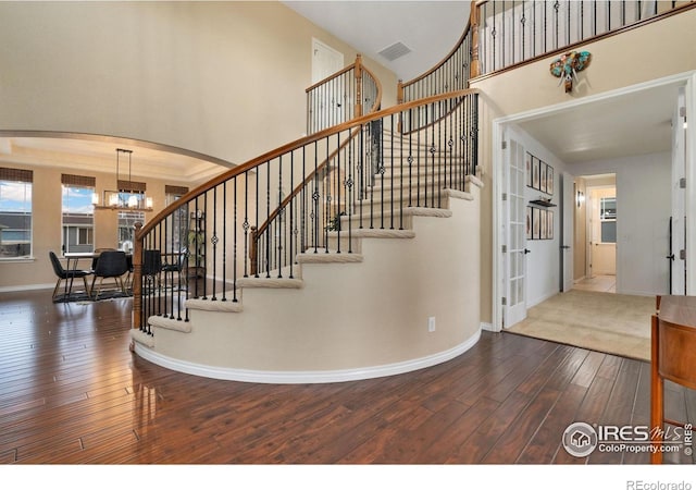 stairway featuring a chandelier, arched walkways, hardwood / wood-style flooring, a towering ceiling, and baseboards