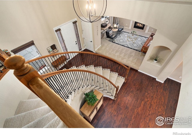 staircase with a notable chandelier, a high ceiling, a glass covered fireplace, wood finished floors, and baseboards