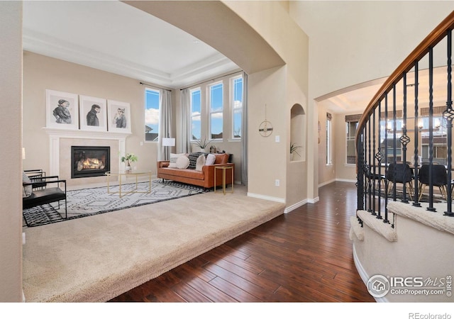 living room featuring arched walkways, dark wood-style flooring, a glass covered fireplace, baseboards, and stairs