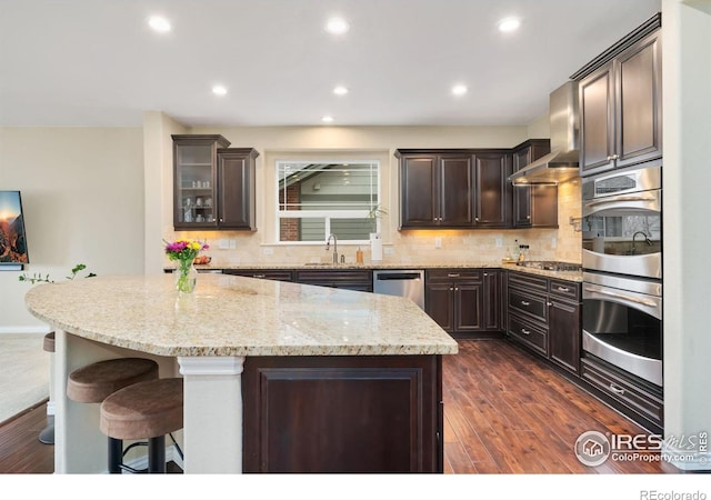 kitchen featuring stainless steel appliances, tasteful backsplash, dark wood-type flooring, dark brown cabinetry, and light stone countertops