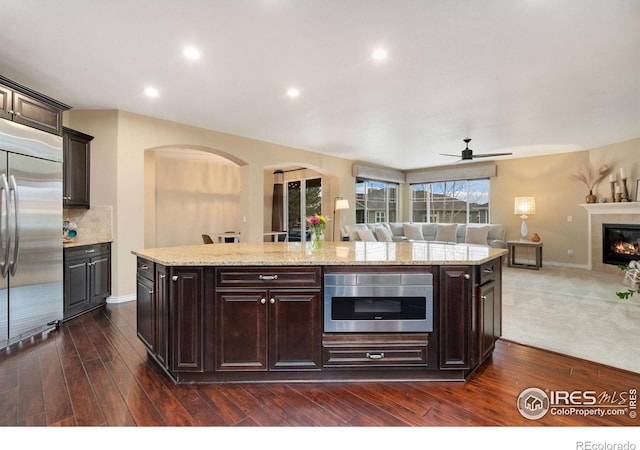 kitchen featuring open floor plan, a tiled fireplace, built in refrigerator, and dark brown cabinets