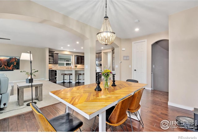 dining area featuring arched walkways, dark wood finished floors, an inviting chandelier, and recessed lighting