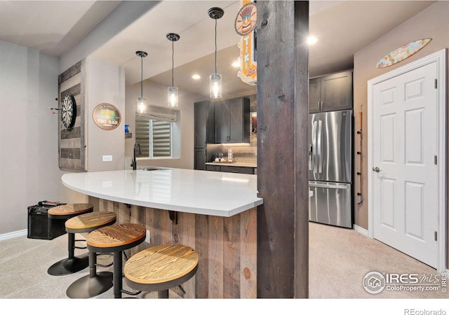 kitchen with stainless steel refrigerator with ice dispenser, a sink, a kitchen bar, and light colored carpet