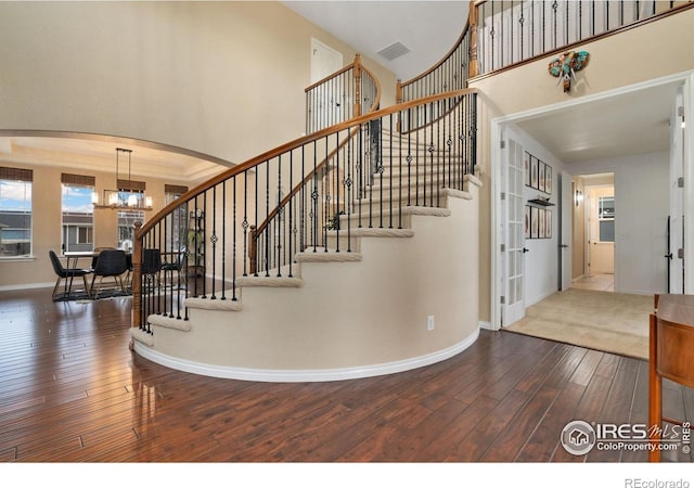 stairs with an inviting chandelier, baseboards, arched walkways, hardwood / wood-style flooring, and visible vents