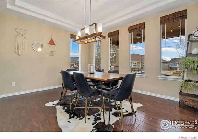 dining room featuring dark wood finished floors, baseboards, a raised ceiling, and an inviting chandelier