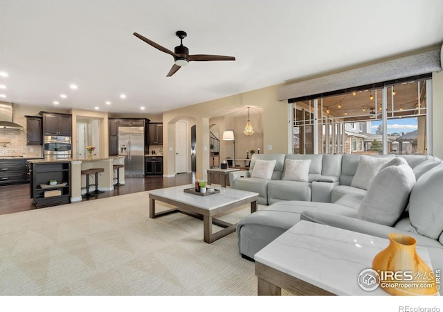 living room with dark wood finished floors, arched walkways, recessed lighting, and a ceiling fan