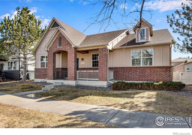 view of front of house featuring a shingled roof, covered porch, fence, board and batten siding, and brick siding